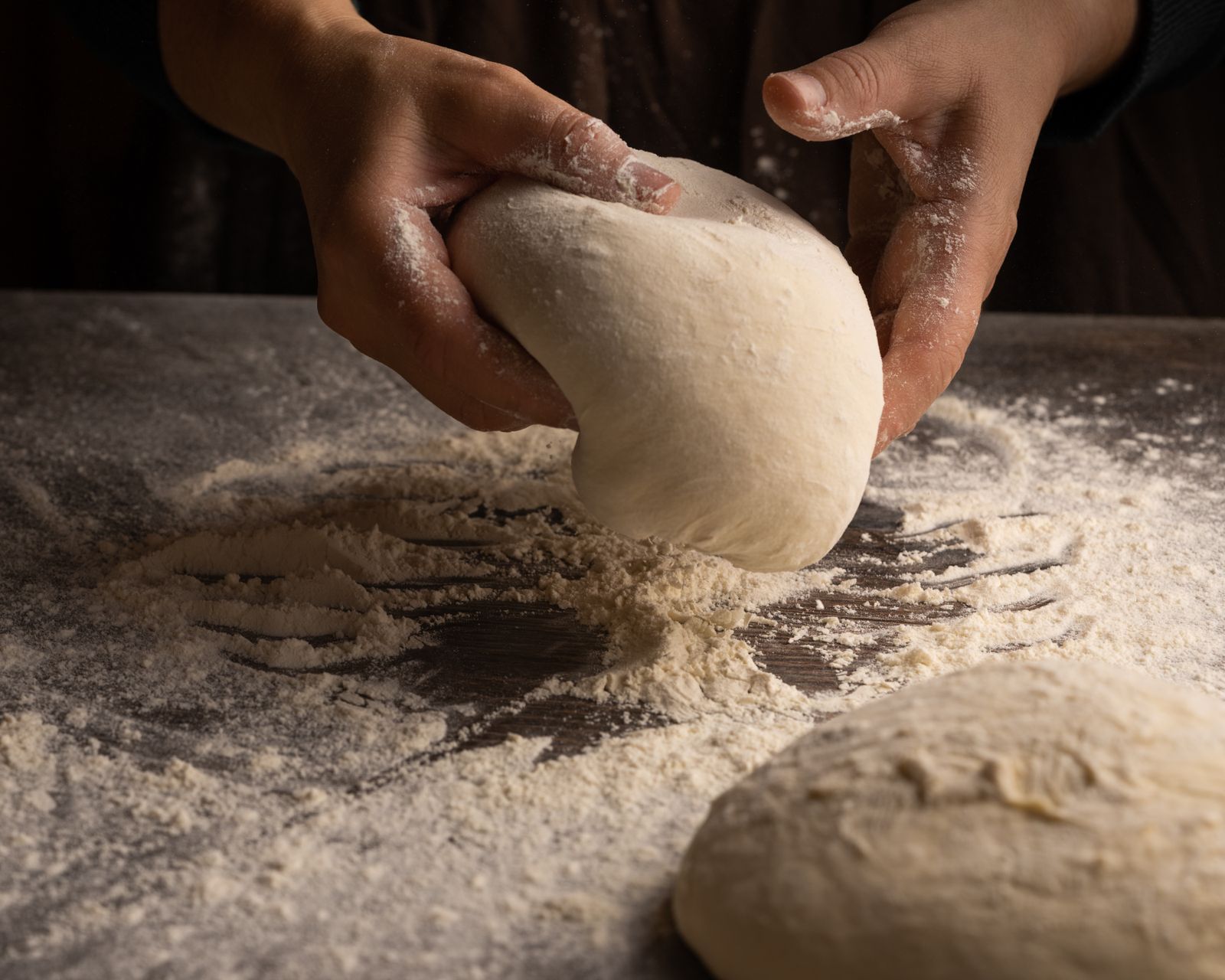 Hands kneading dough on a floured surface, capturing artisan bread making.