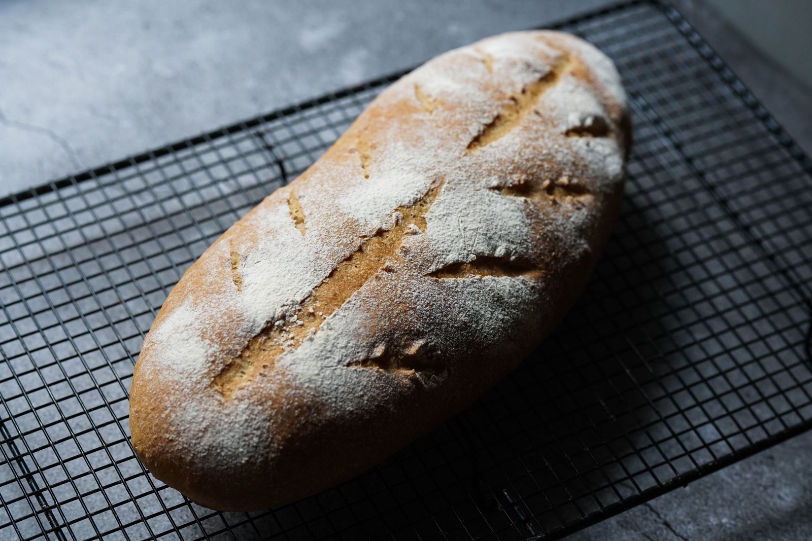 A finished country sourdough loaf with a dark crust, cooling on a rack