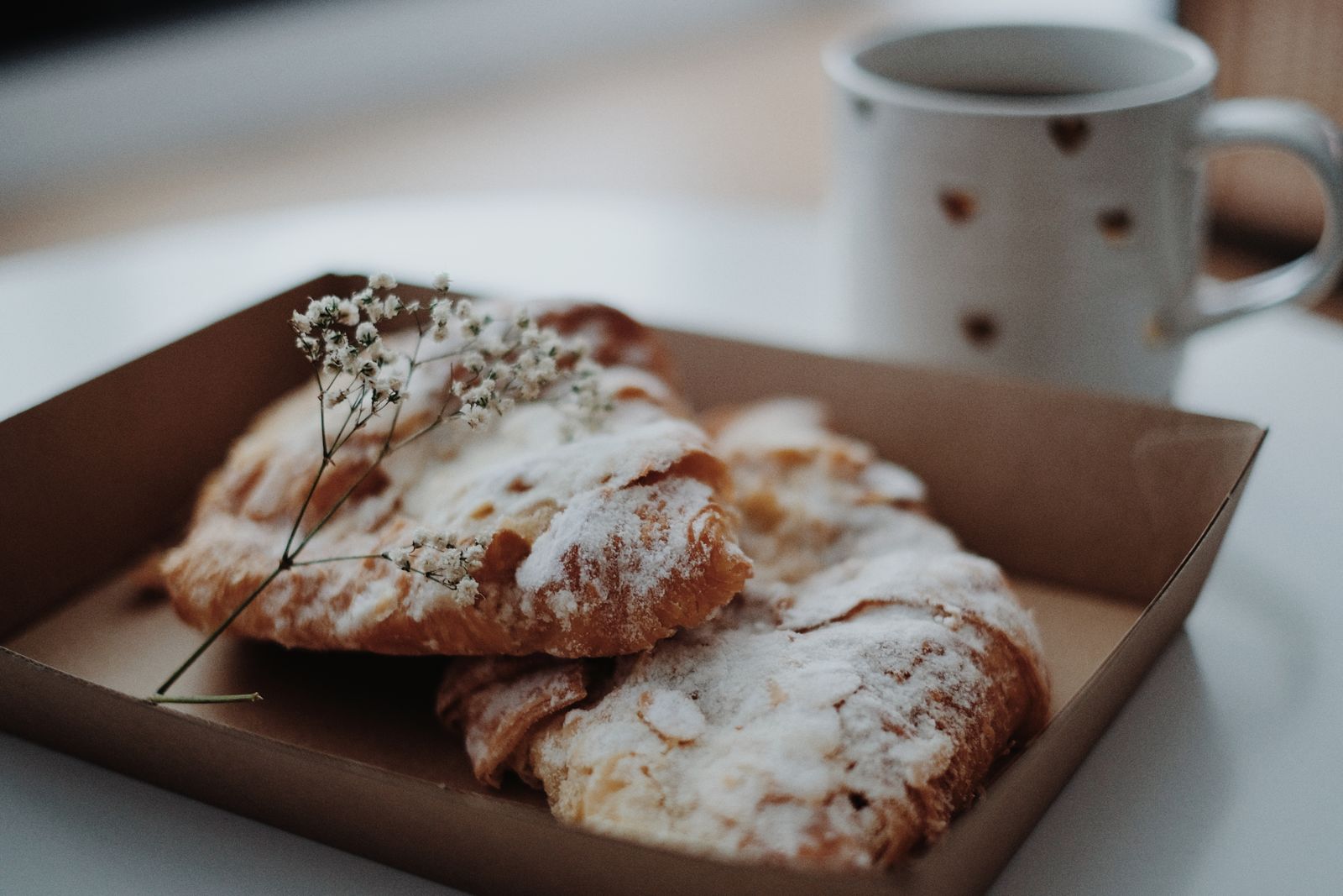 A pair of sugar-dusted croissants next to a coffee cup in a relaxed indoor setting.