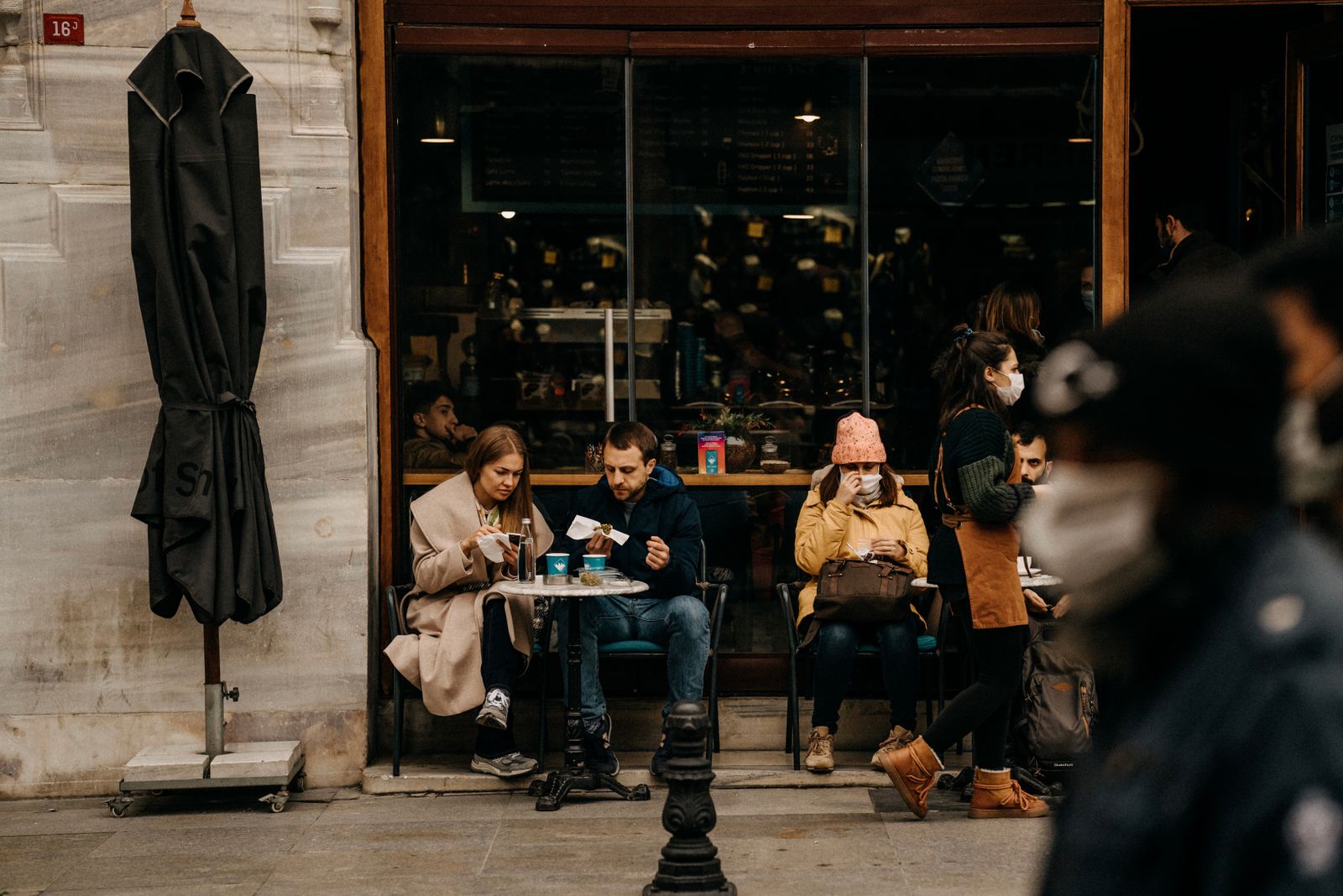 People enjoying meals and coffee outside a café with a bustling sidewalk scene.