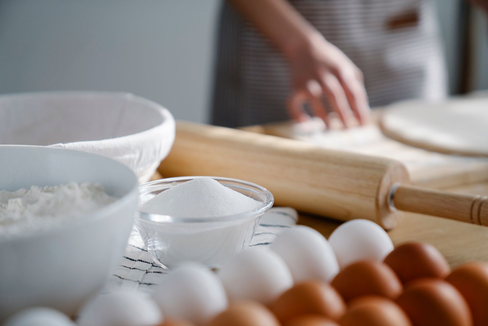 Close-up image of baking ingredients with rolling pin and dough being prepared.